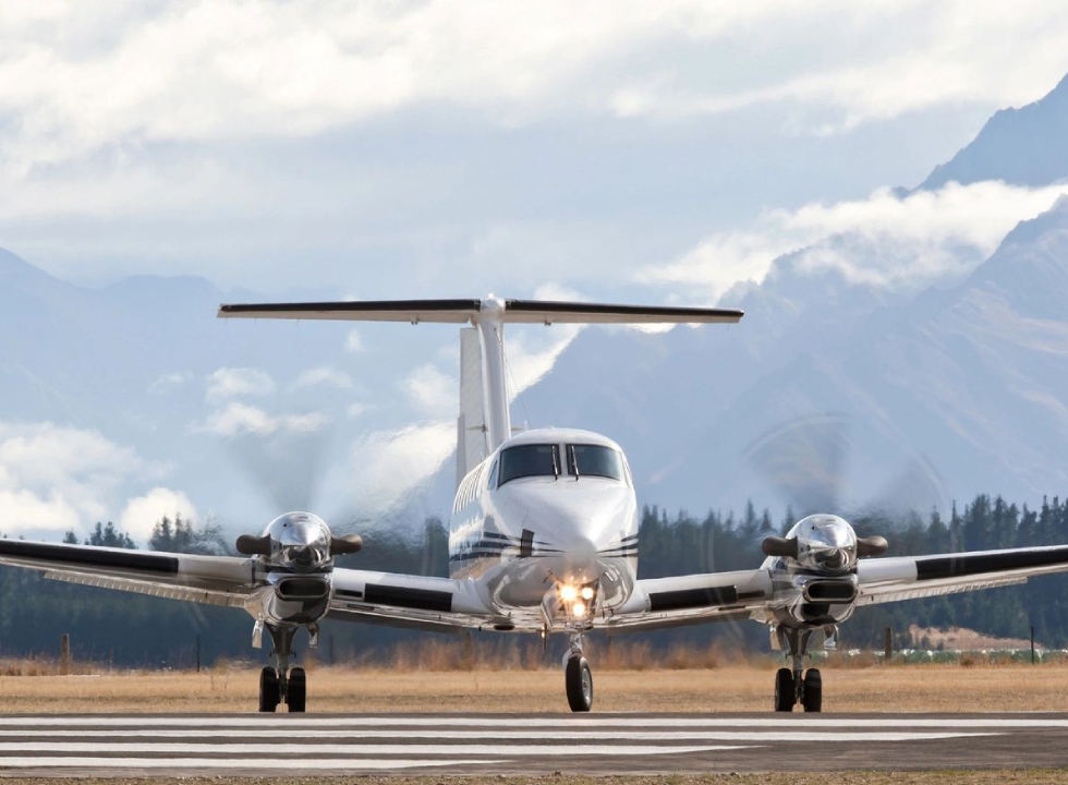 A small plane is on the runway with mountains in the background.